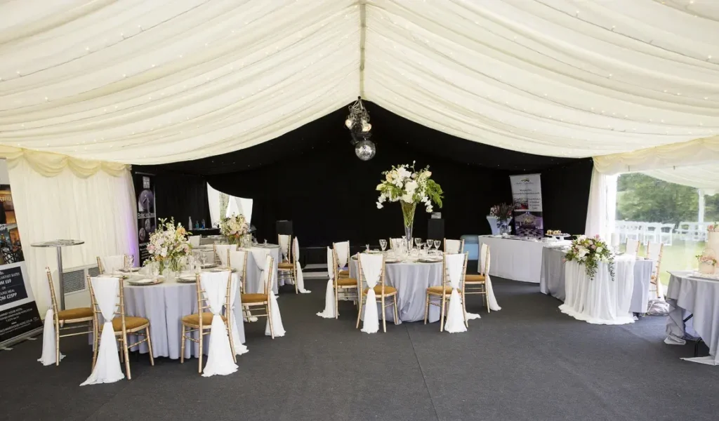 Elegant corporate event marquee with round tables set for dining, featuring white linens, floral centerpieces, and draped ceilings.