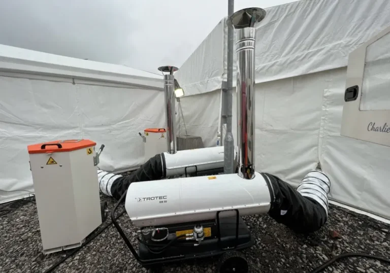Two marquee heaters by Melody Corporation and flexible ducts outside a white tent, suggesting a setup for heating or ventilation.