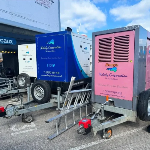 Two trailer-mounted generators, one blue and one pink, are parked side by side in a lot. Both are branded “Melody Corporation” and are secured with wheel locks. Two trailer-mounted generators, one blue and one pink, are parked side by side in a lot. Both are branded "Melody Corporation" and are secured with wheel locks.