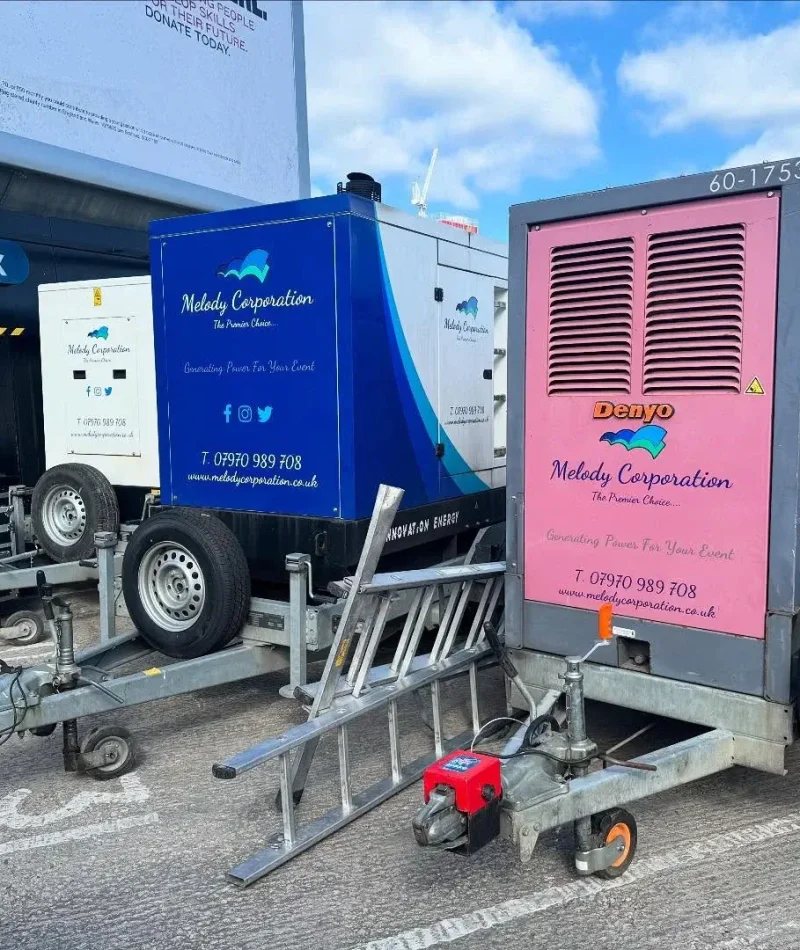 Two trailer-mounted generators, one blue and one pink, are parked side by side in a lot. Both are branded "Melody Corporation" and are secured with wheel locks.